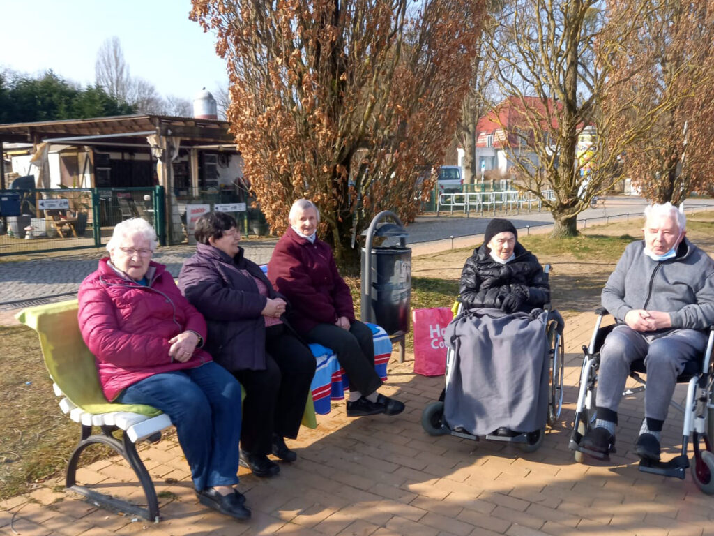 Gruppe älterer Menschen im Freien auf Bänken sitzend