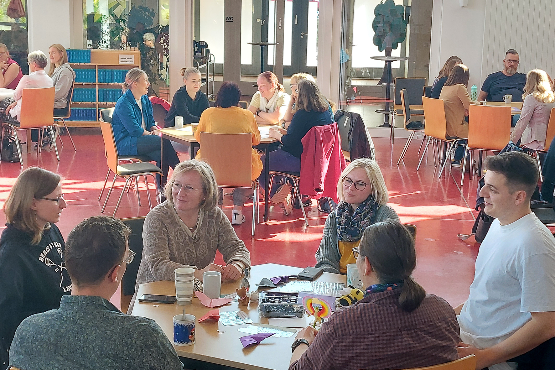 Gruppentreffen in einem Gemeinschaftsraum mit Personen an Tischen bei Gesprächen.