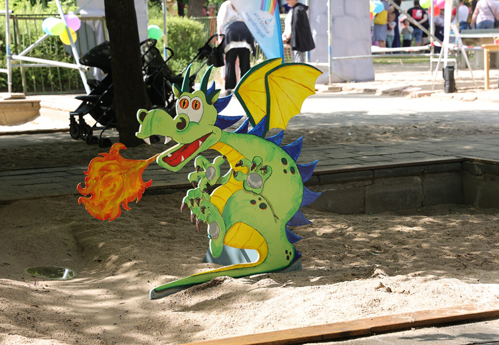Ein bunter Pappdrache in einem Sandkasten spuckt eine Flamme.