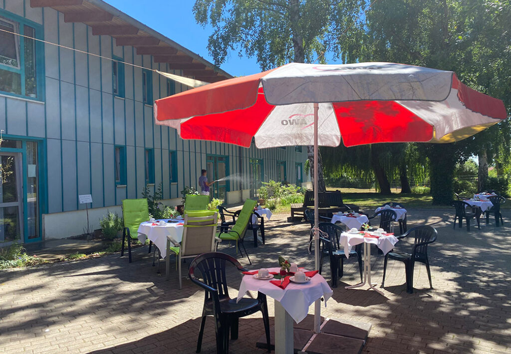 Außenbereich eines Cafés mit großen Sonnenschirmen und gedeckten Tischen.