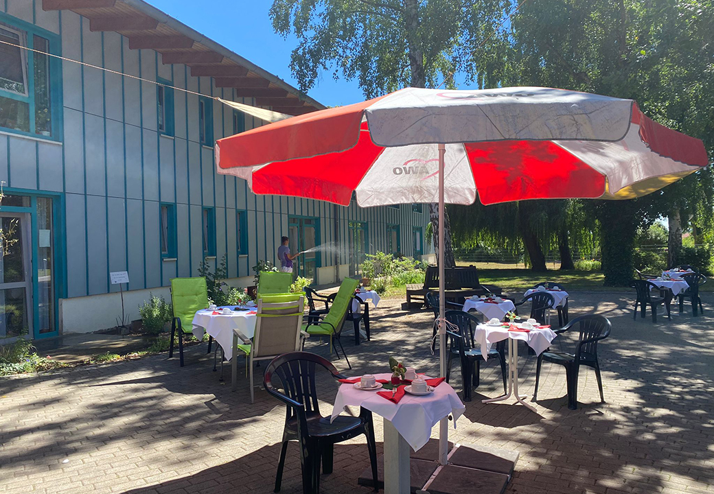 Außenbereich eines Cafés mit großen Sonnenschirmen und gedeckten Tischen.
