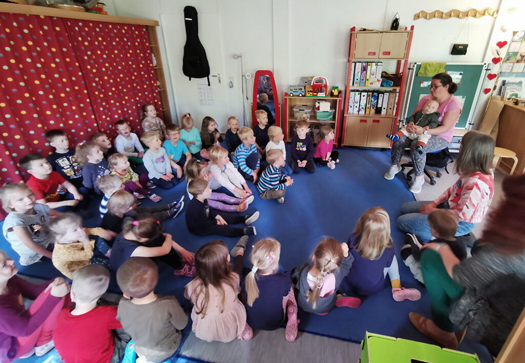 Gruppe von Kindern und Erwachsenen in einem Raum mit rotem Vorhang