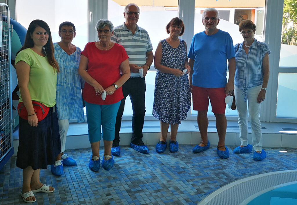 Gruppe von sieben Personen in einem Innenraum mit blauen &Uuml;berziehschuhen.