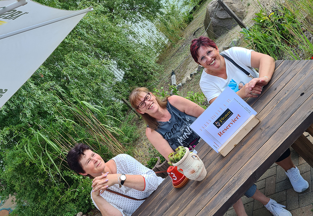 Drei Frauen sitzen an einem Holztisch im Freien.
