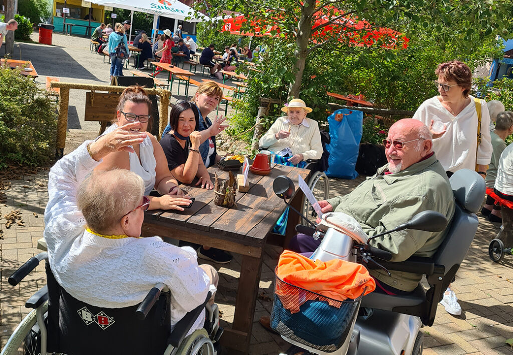 Eine Gruppe von Menschen trifft sich im Freien an einem Holztisch.