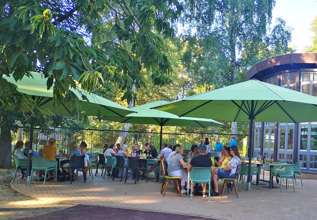 Eine Gruppe von Menschen sitzt unter gr&uuml;nen Sonnenschirmen an Tischen im Freien.