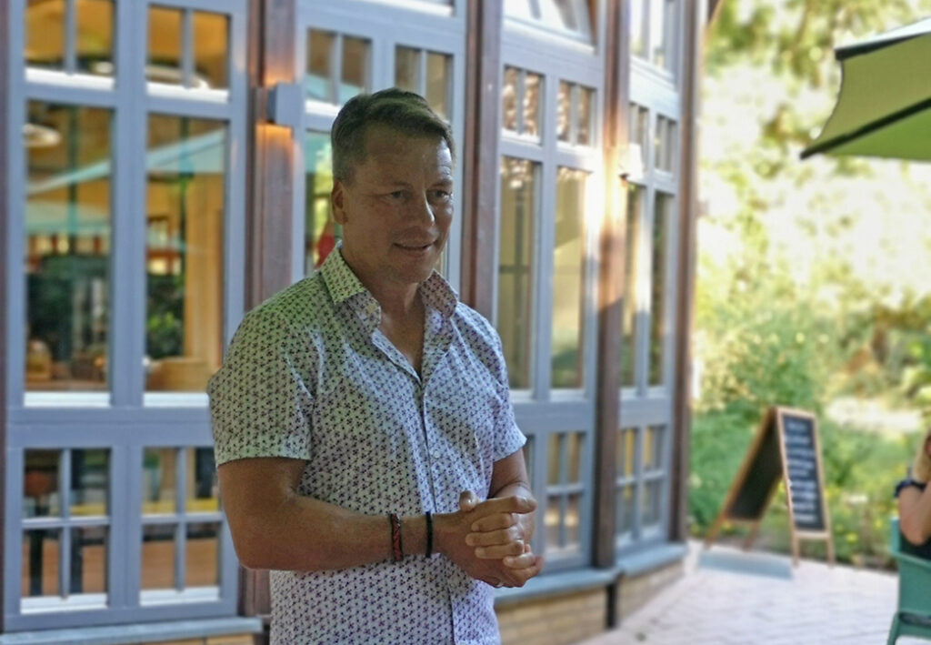 Ein Mann steht vor einem Geb&auml;ude mit gro&szlig;en Fenstern und h&auml;lt seine H&auml;nde zusammen.