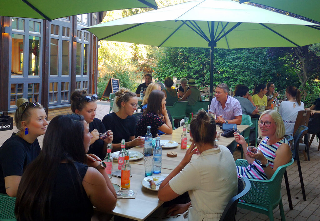 Eine Gruppe von Menschen sitzt im Freien an einem Tisch unter gro&szlig;en Sonnenschirmen.