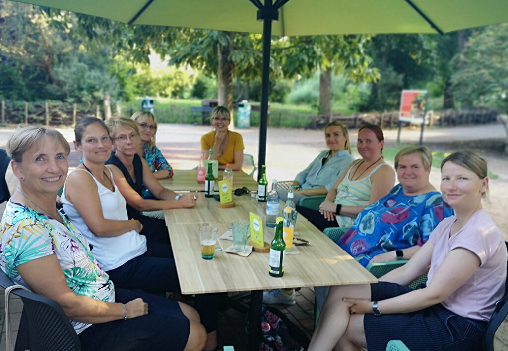 Eine Gruppe von zehn Frauen sitzt um einen Tisch im Freien.