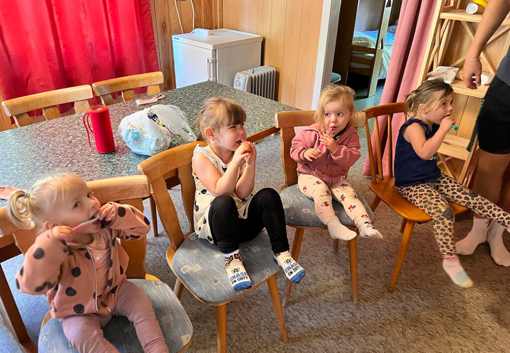 Vier Kleinkinder sitzen auf St&uuml;hlen und putzen gemeinsam ihre Z&auml;hne.