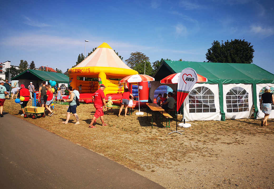 Ein Freiluftfest mit einem gelben aufblasbaren Spielgerät, mehreren Pavillons und Menschen.