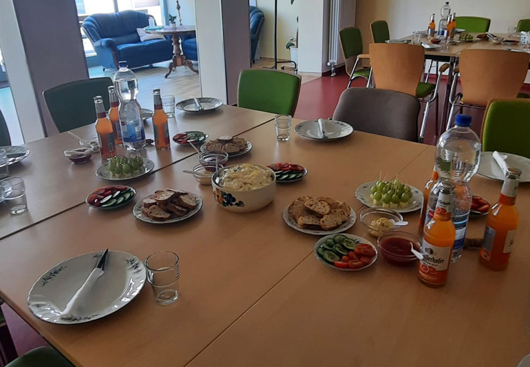 Ein gedeckter Tisch in einem Gemeinschaftsraum mit Speisen und Getränken.