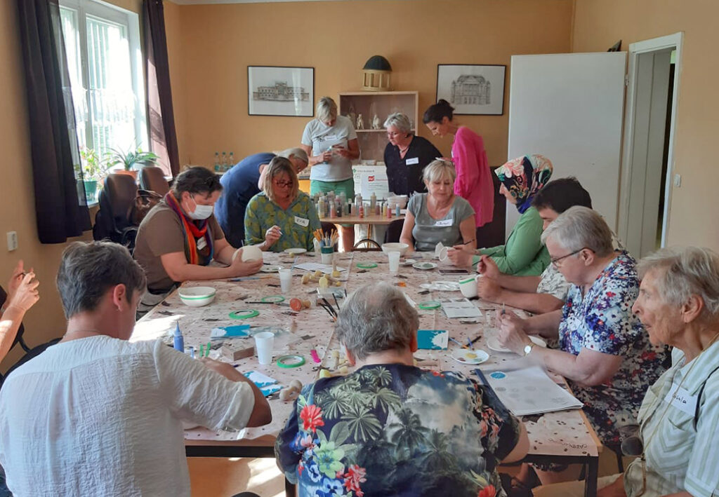 Menschen sitzen in einem Raum um einen Tisch und nehmen gemeinsam an einer kreativen Aktivit&auml;t teil.