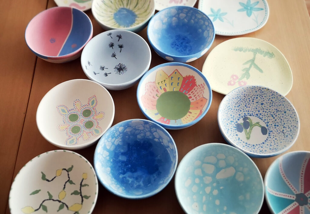 Handgemalte Sch&uuml;sseln in verschiedenen Designs auf einem Holztisch.