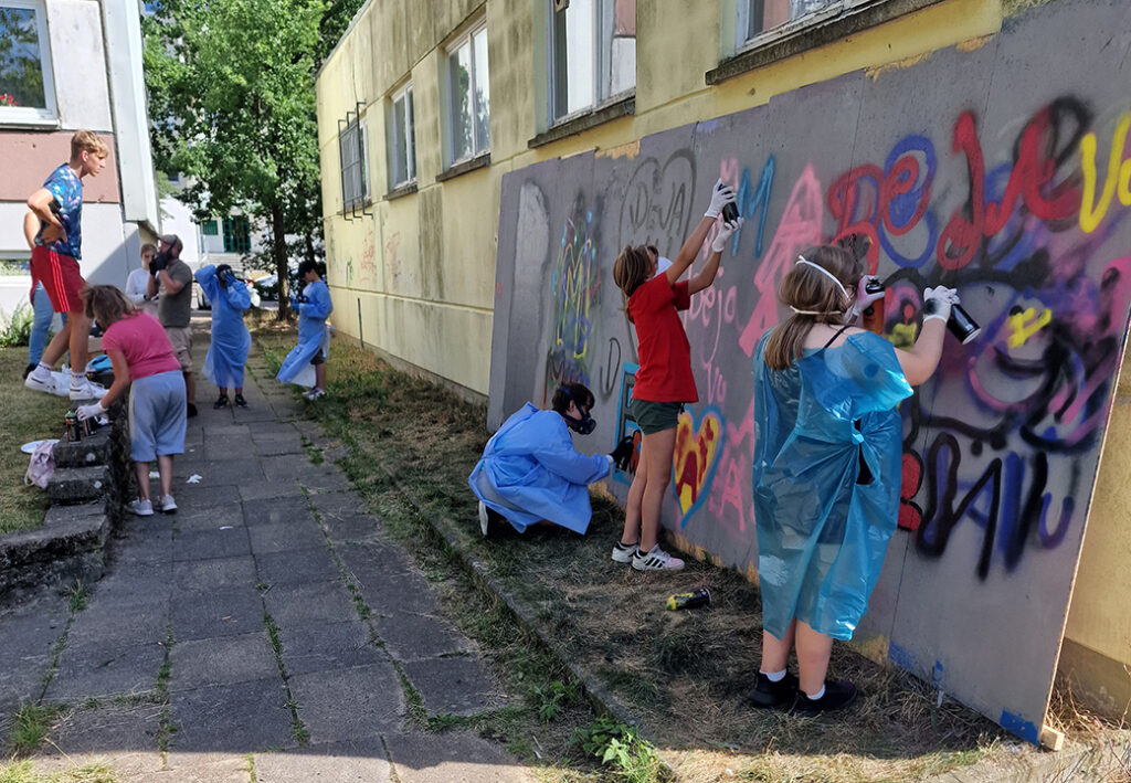 Personen beim Graffiti-Sprayen an der Wand eines Geb&auml;udes.