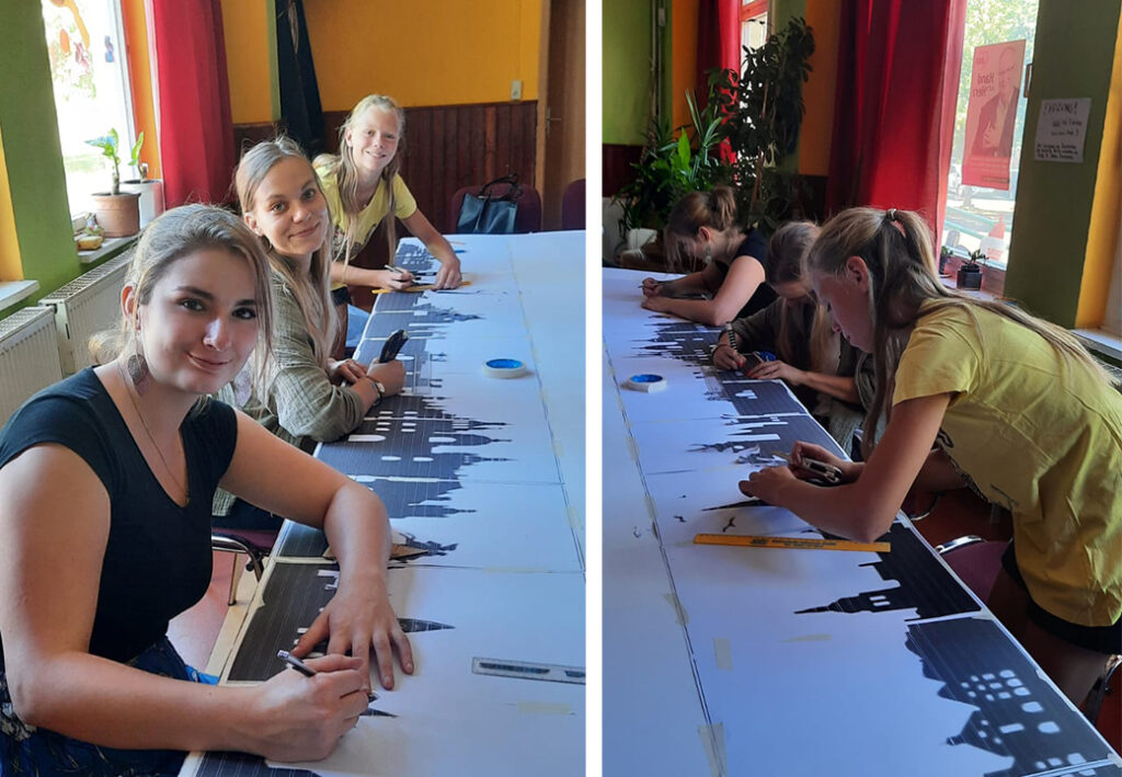 Gruppe von jungen Frauen bei der kreativen Arbeit an einem langen Tisch.