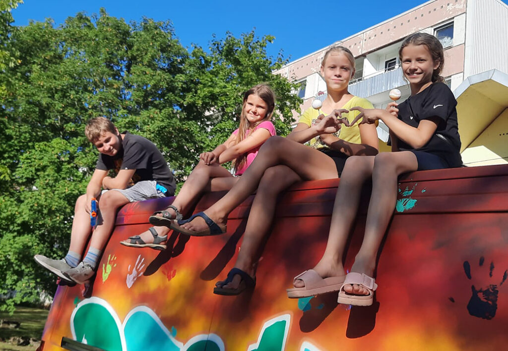 Vier lachende Kinder sitzen auf einem bunten Fahrzeugdach.
