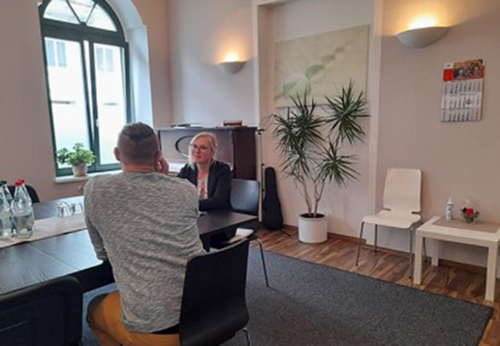 Zwei Personen sitzen sich an einem Tisch gegen&uuml;ber in einem B&uuml;ro.