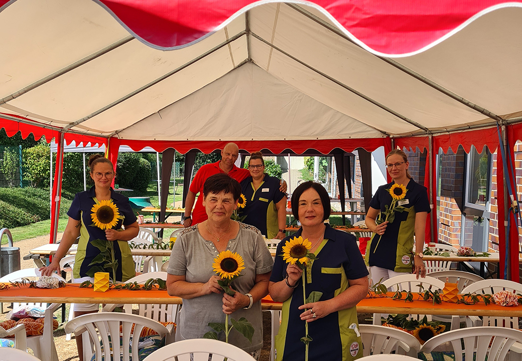 Gruppe von Menschen in einem Zelt mit Sonnenblumen in den Händen
