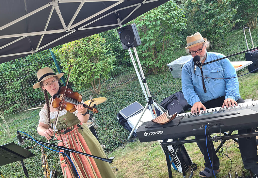 Ein Mann und eine Frau musizieren unter einem Pavillon im Freien.