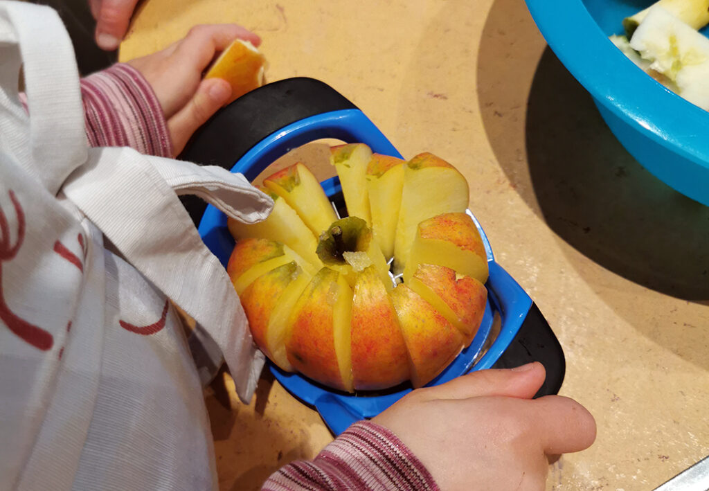 Kind schneidet einen Apfel mit einem Apfelschneider.