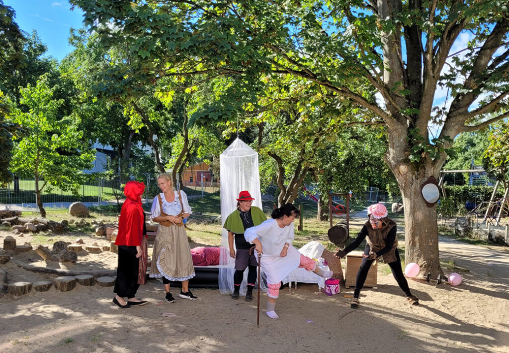 Eine Gruppe von Menschen in Kost&uuml;men f&uuml;hrt eine Theaterszene im Freien auf.