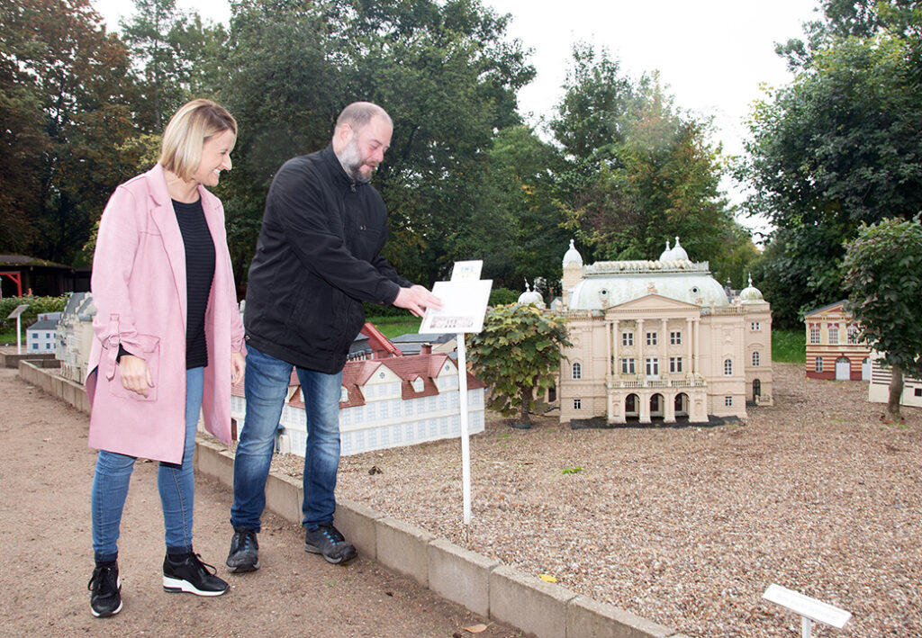 Zwei Personen betrachten ein Miniaturmodell eines Geb&auml;udes im Freien.