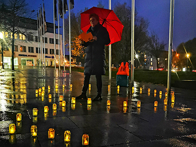 Person mit rotem Regenschirm zwischen leuchtenden Kerzen im Freien