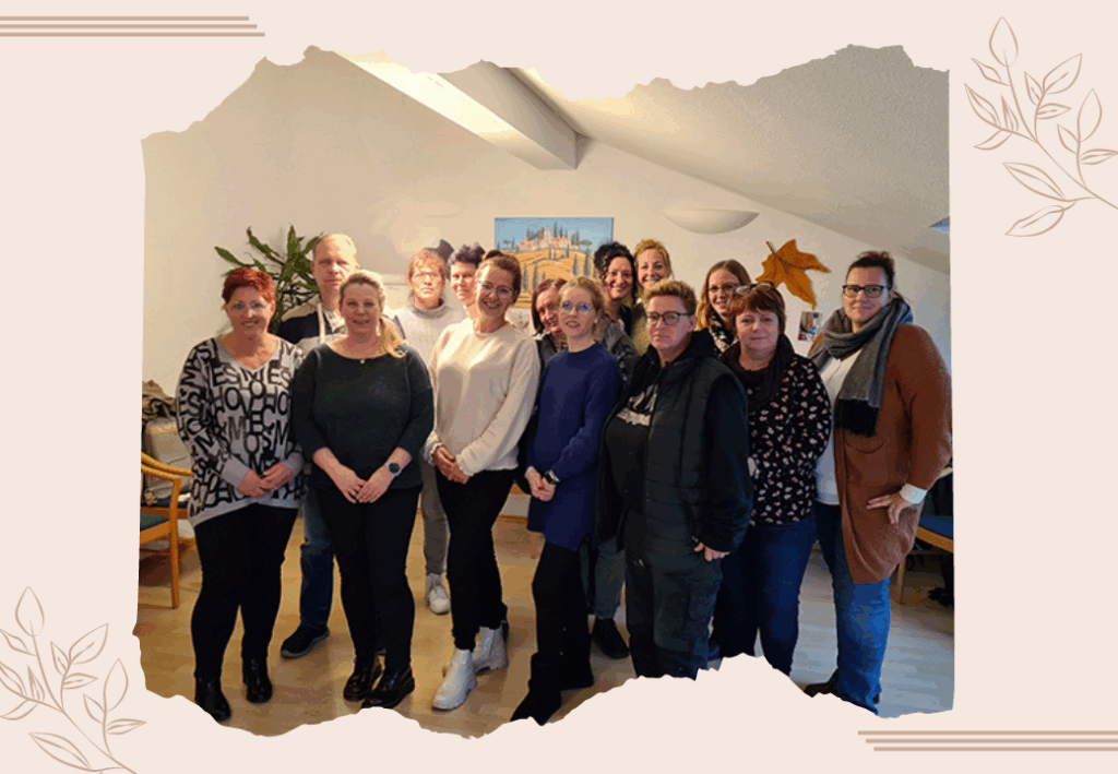 Eine Gruppe von 13 Menschen steht in einem hellen Raum nebeneinander und lächelt in die Kamera.