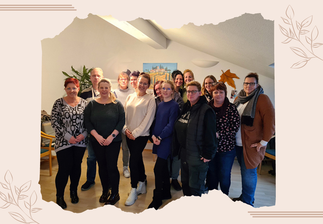 Eine Gruppe von 13 Menschen steht in einem hellen Raum nebeneinander und lächelt in die Kamera.