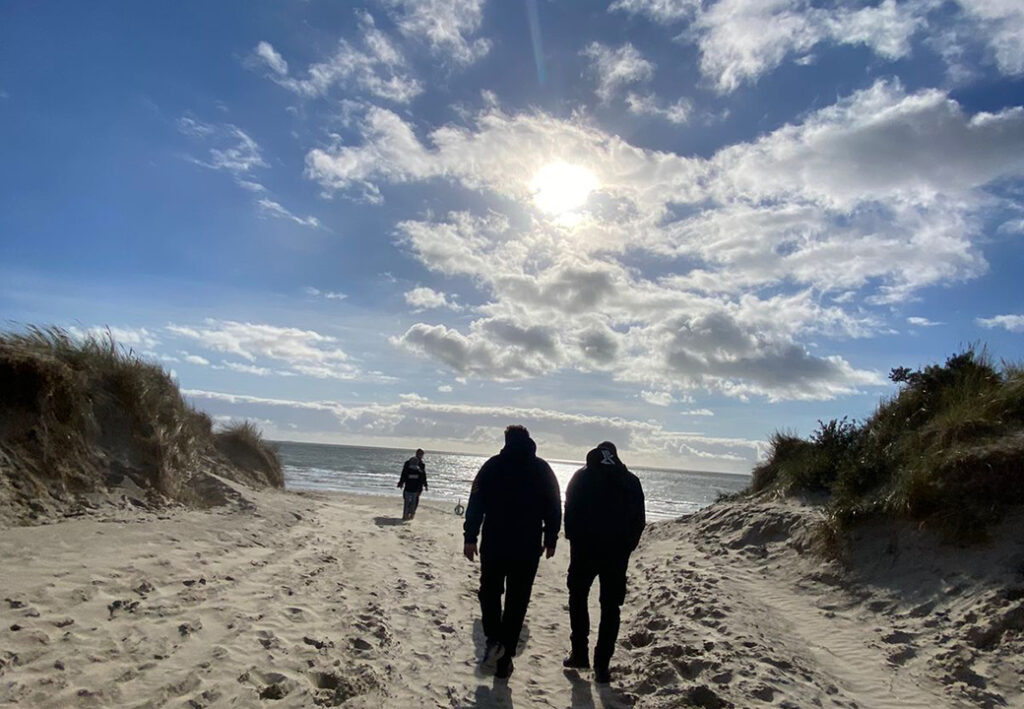 Drei Personen gehen am Strand entlang.