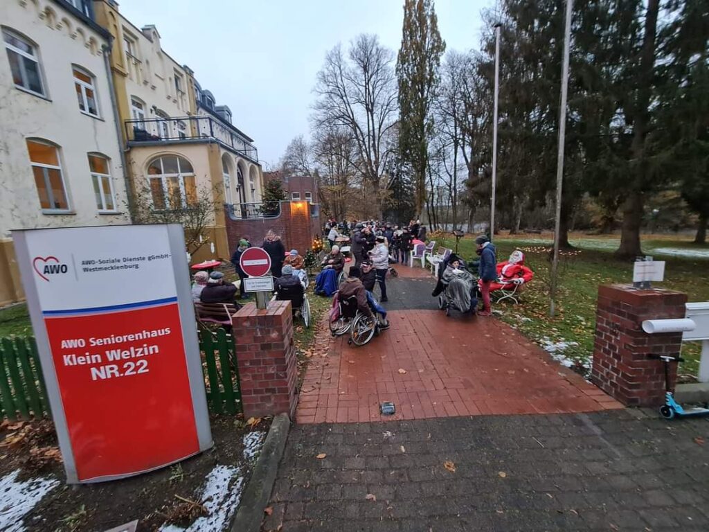 Eine Gruppe von Menschen versammelt sich auf einem Weg vor einem Seniorenheim der AWO in winterlicher Umgebung.