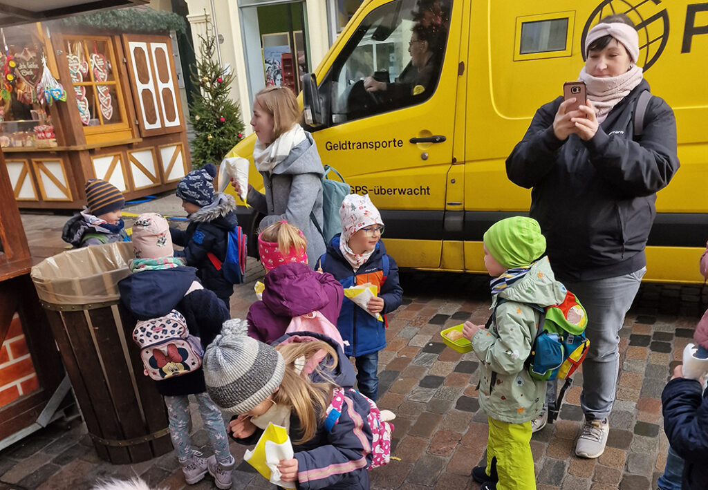 Gruppe von Kindern und Erwachsenen auf einem Weihnachtsmarkt vor einem gelben Transporter.