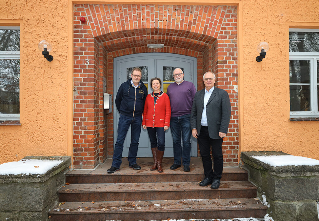 Vier Personen stehen vor einem Gebäude mit Ziegelsteinfassade.