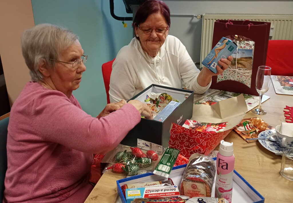 Zwei &auml;ltere Frauen sitzen an einem Tisch mit offenen Geschenkboxen vor sich.
