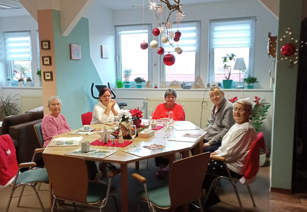 Mehrere &auml;ltere Frauen sitzen an einem weihnachtlich dekorierten Tisch in einem Gemeinschaftsraum.