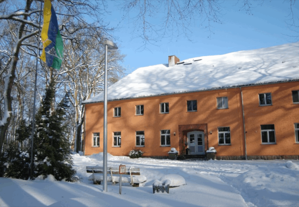 Ein zweist&ouml;ckiges Geb&auml;ude im Winter mit oranger Fassade und schneebedecktem Dach.