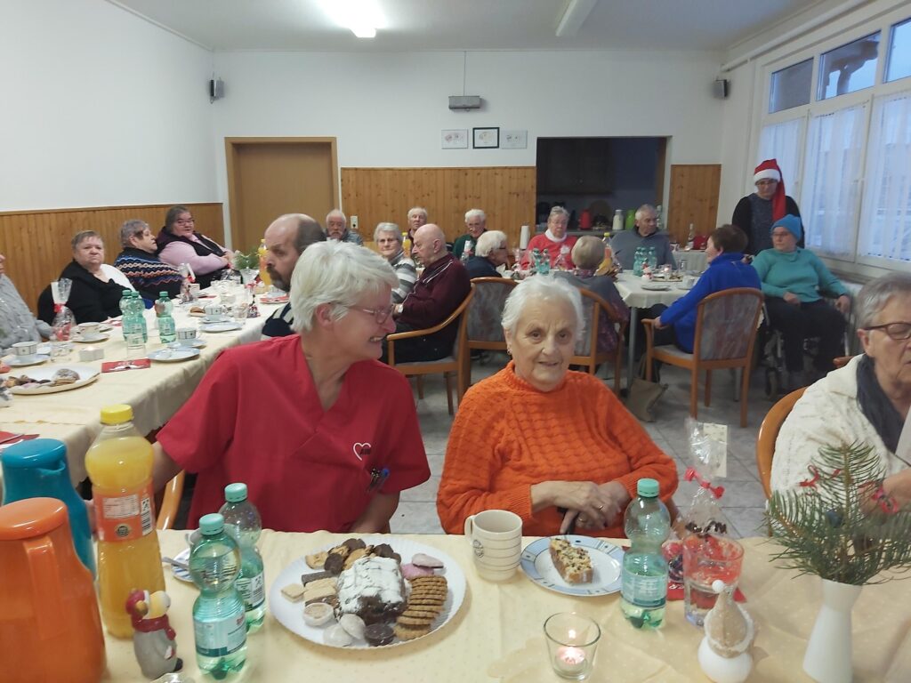Eine Gruppe von älteren Menschen sitzt an festlich gedeckten Tischen in einem Raum.