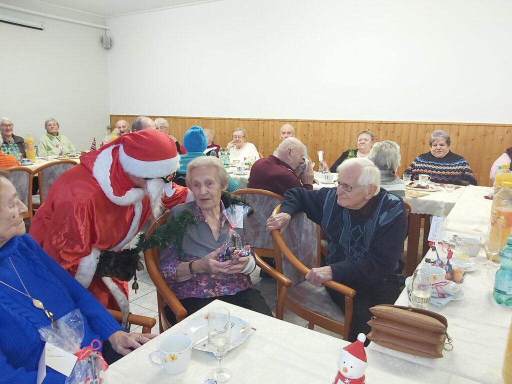 &Auml;ltere Menschen sitzen in einem Gemeinschaftsraum bei einer weihnachtlichen Feier zusammen.