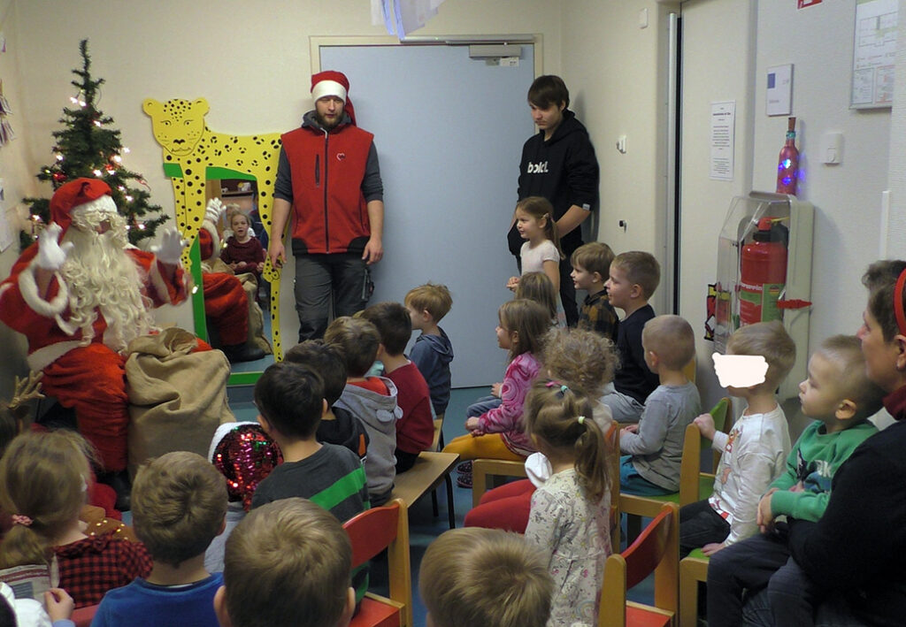 Kinder sitzen auf St&uuml;hlen vor einem Weihnachtsmann und Erwachsenen, die eine Geschichte erz&auml;hlen.