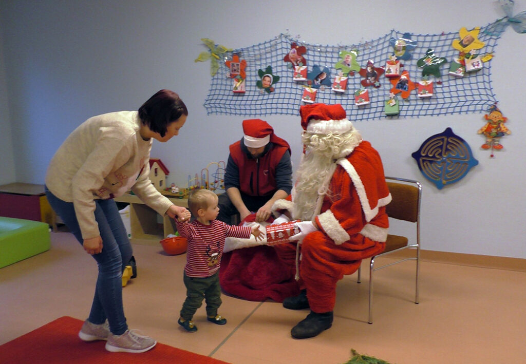 Ein kleines Kind bekommt ein Geschenk vom Weihnachtsmann in einem Raum mit Weihnachtsschmuck.