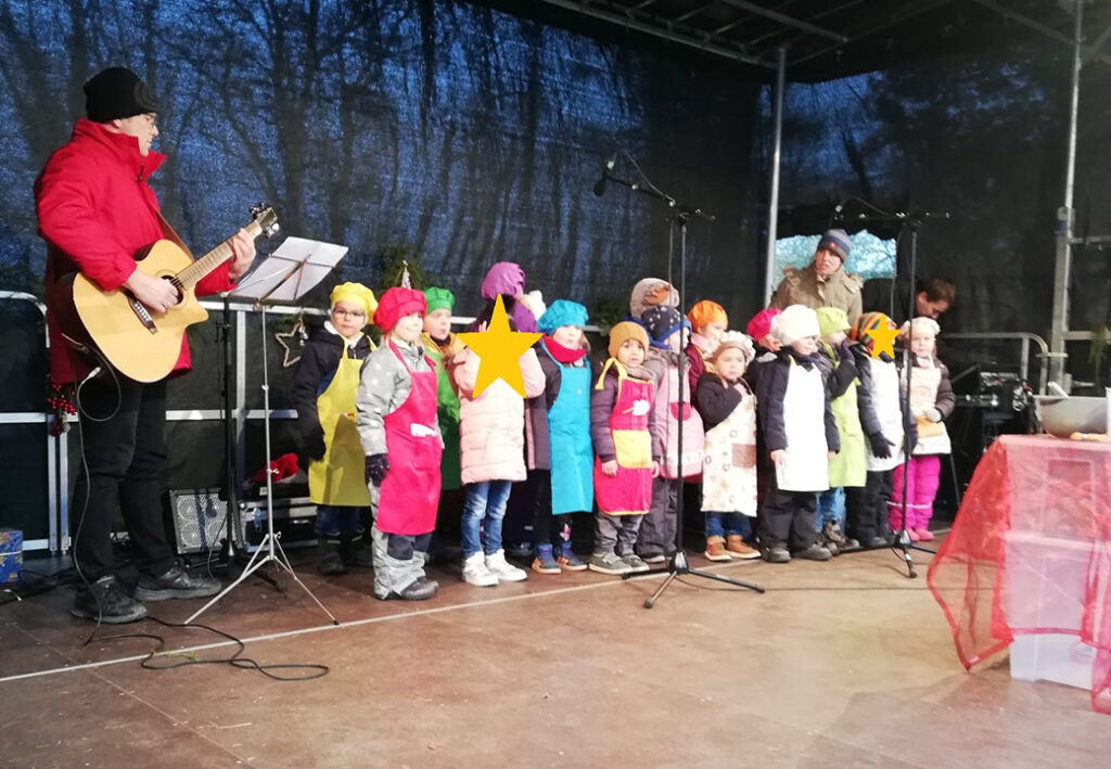 Kinder stehen auf einer B&uuml;hne mit einem Gitarristen