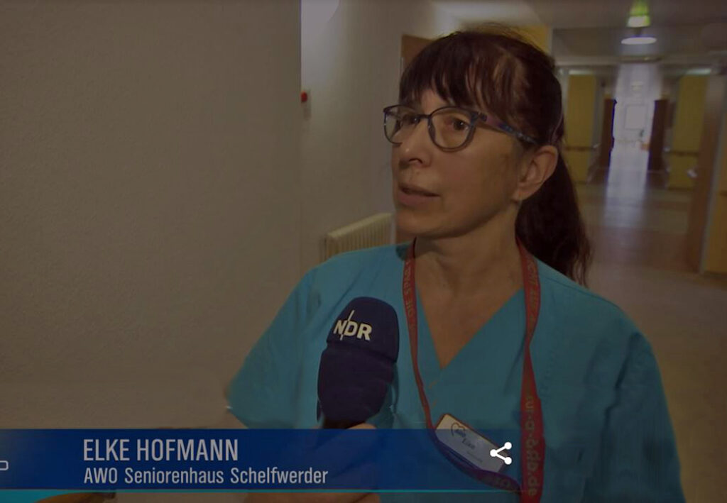 Eine Frau in blauer Arbeitskleidung mit NDR-Mikrofon