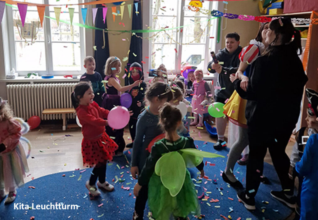 Kinder und Erwachsene bei einer Feier in einem Raum mit bunten Girlanden und Konfetti.