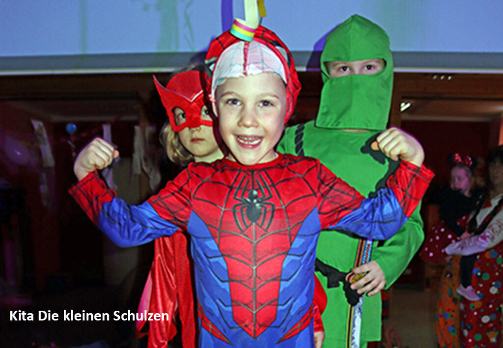 Drei Kinder in farbenfrohen Kost&uuml;men posieren fr&ouml;hlich.