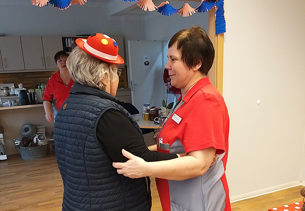 Zwei Personen in einem Raum, die sich freundlich unterhalten. Eine Person trägt eine rote Uniform, die andere person einen dekorativen roten Hut.