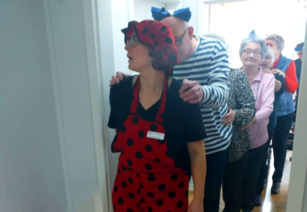 Eine Gruppe von Menschen, die eine Polonaise bilden. Die vorderste Person tr&auml;gt ein rot-schwarz gepunktetes Kost&uuml;m und Hut.