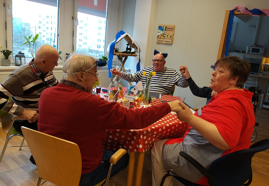 Eine Gruppe von Personen sitzt an einem Tisch und feiert fr&ouml;hlich mit Partykegeln und Dekorationen.