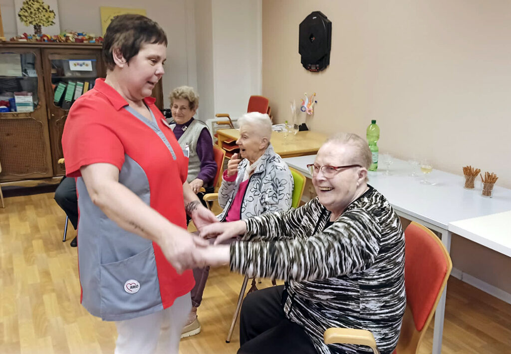 Eine Betreuerin interagiert mit &auml;lteren Menschen in einem Gemeinschaftsraum.
