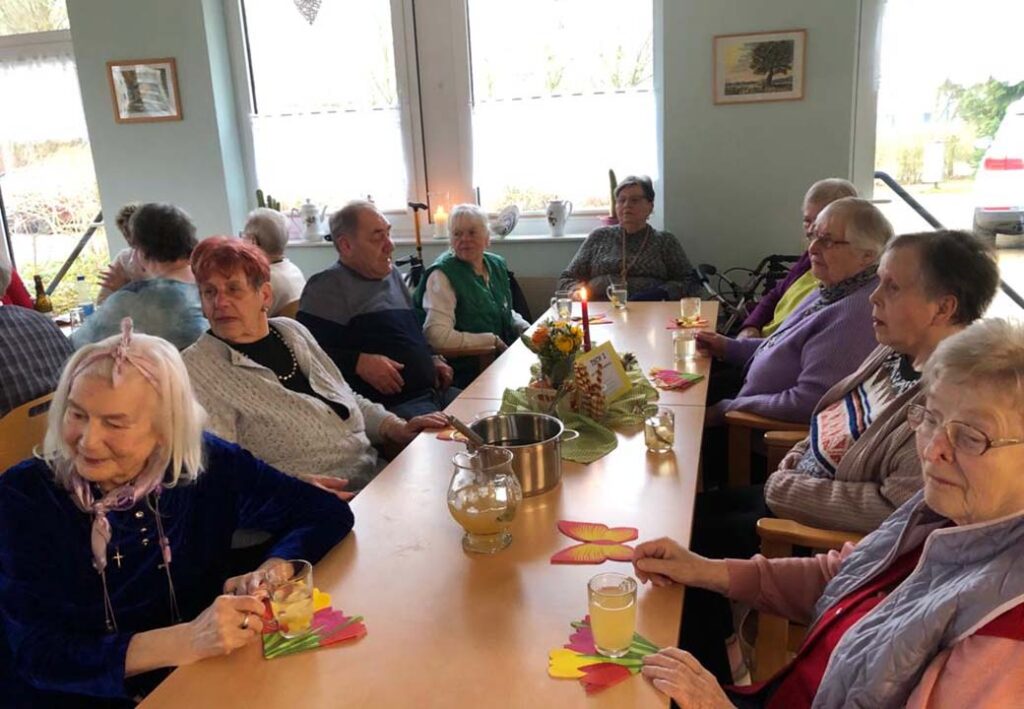 Gruppe von Senioren an einem Tisch in einem Gemeinschaftsraum.